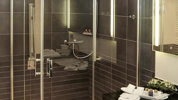 A modern bathroom with a glass-enclosed shower, dark tiled walls, and a vanity with a mirror.