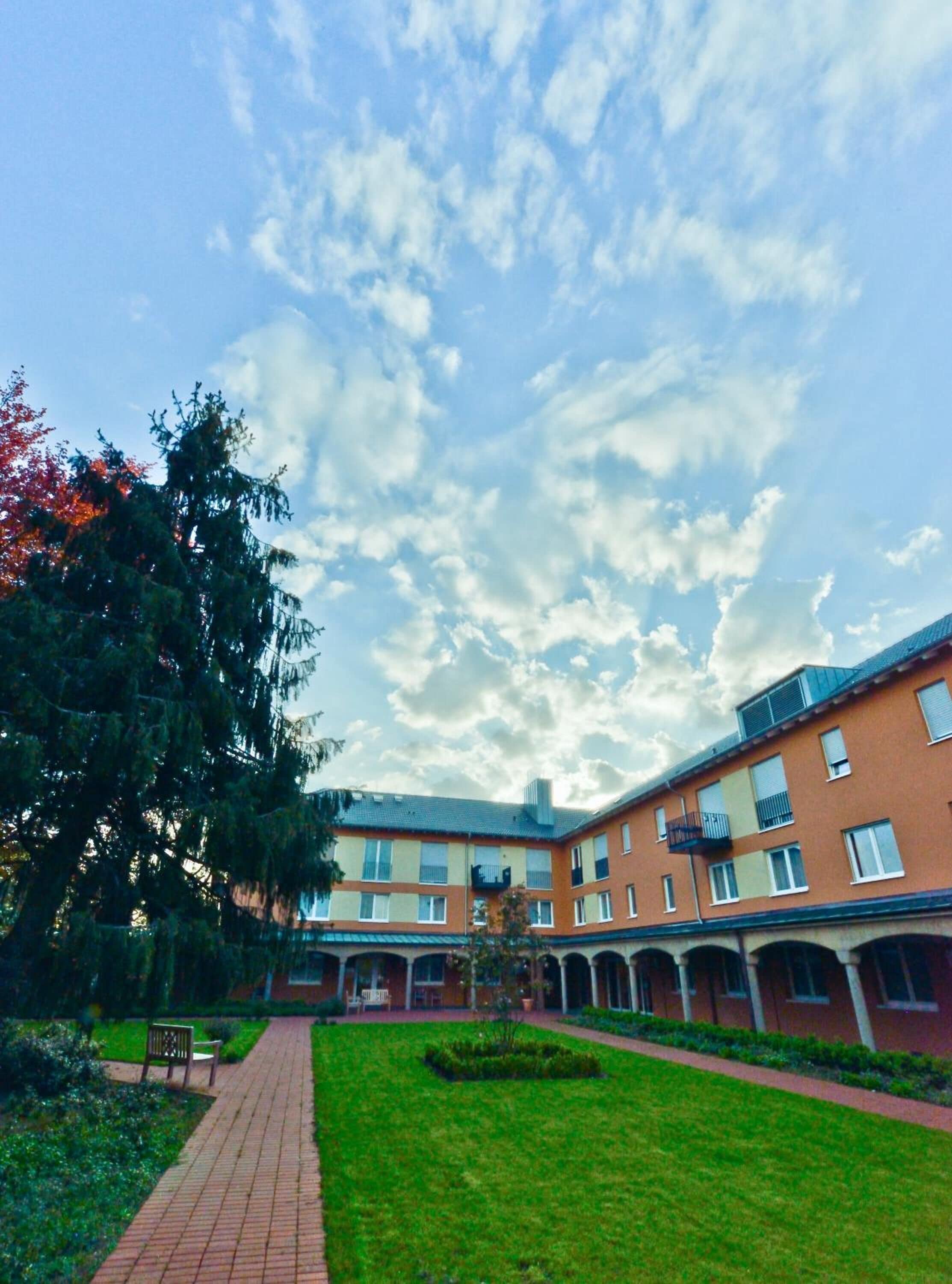 Un patio con sendero de ladrillo, césped verde y un edificio de varios pisos con balcones.