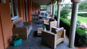 An outdoor patio with wooden furniture, including sofas and chairs, arranged around tables. - Hotel Klostergarten (Kevelaer)