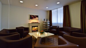 A modern living room with a fireplace, leather sofas, a coffee table, and a wine rack. - Hotel Klostergarten (Kevelaer)