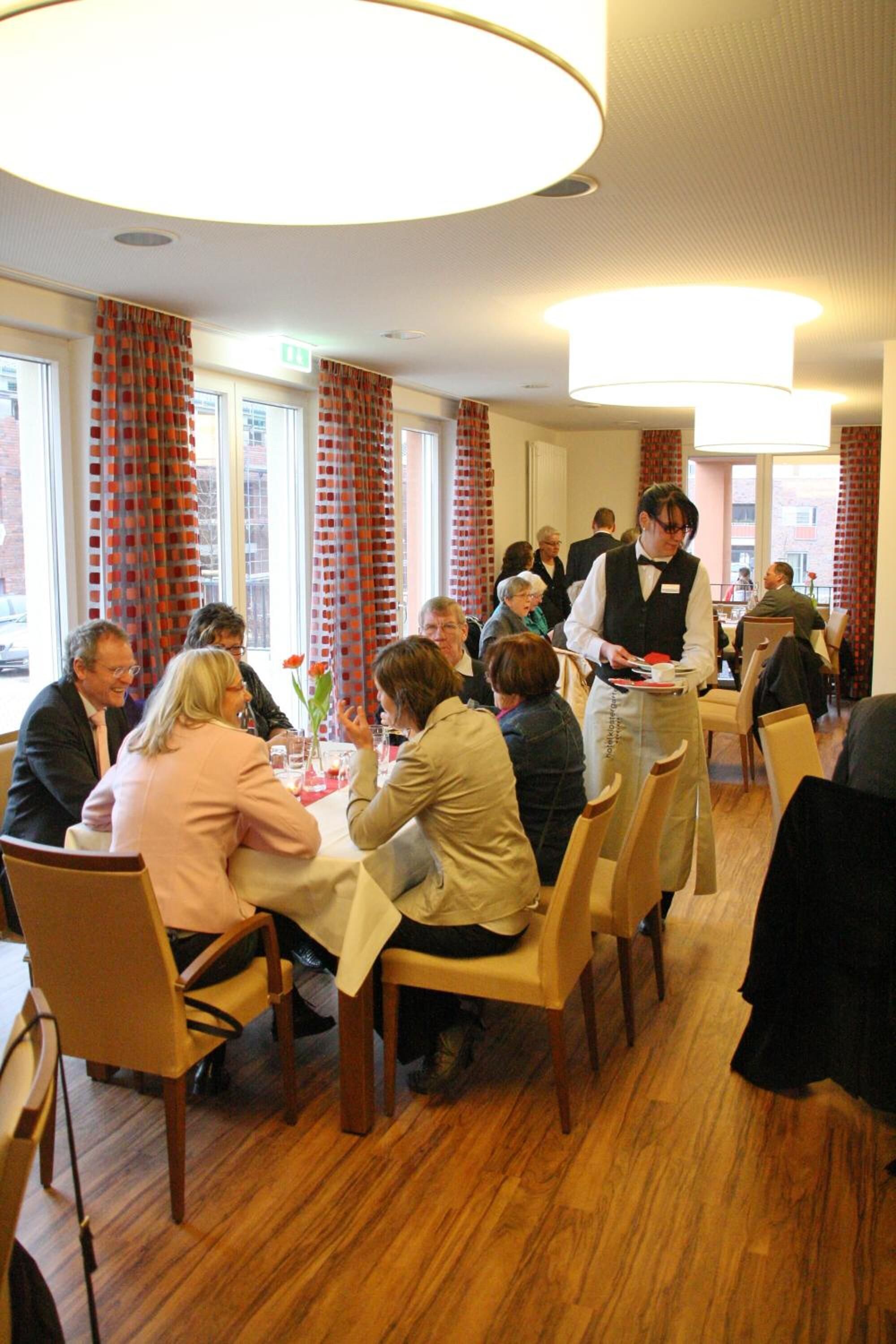A restaurant with wooden flooring, round tables, and red curtains.