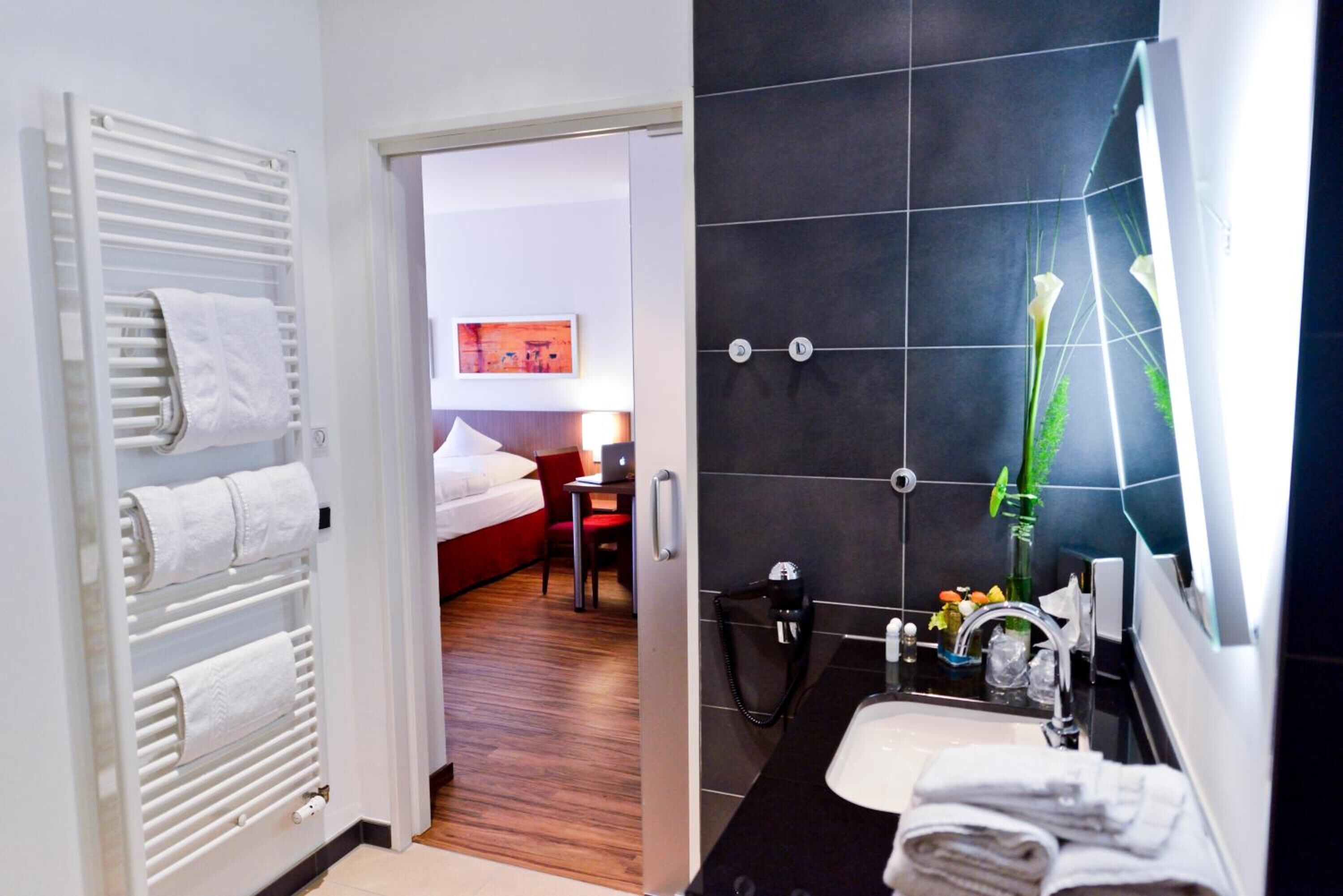 Ein Hotelzimmer mit Bett, Schreibtisch, Stuhl, Bad mit Waschbecken und Handtuchhalter.
