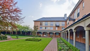 A courtyard with a brick pathway, a lawn, and a building with multiple windows and balconies. - Hotel Klostergarten (Kevelaer)