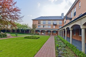 Um pátio com caminho de tijolos, gramado e um edifício com várias janelas e varandas.