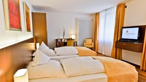 A hotel room with a large bed, a desk with a chair, a television, and a window with curtains. - Hotel Klostergarten (Kevelaer)