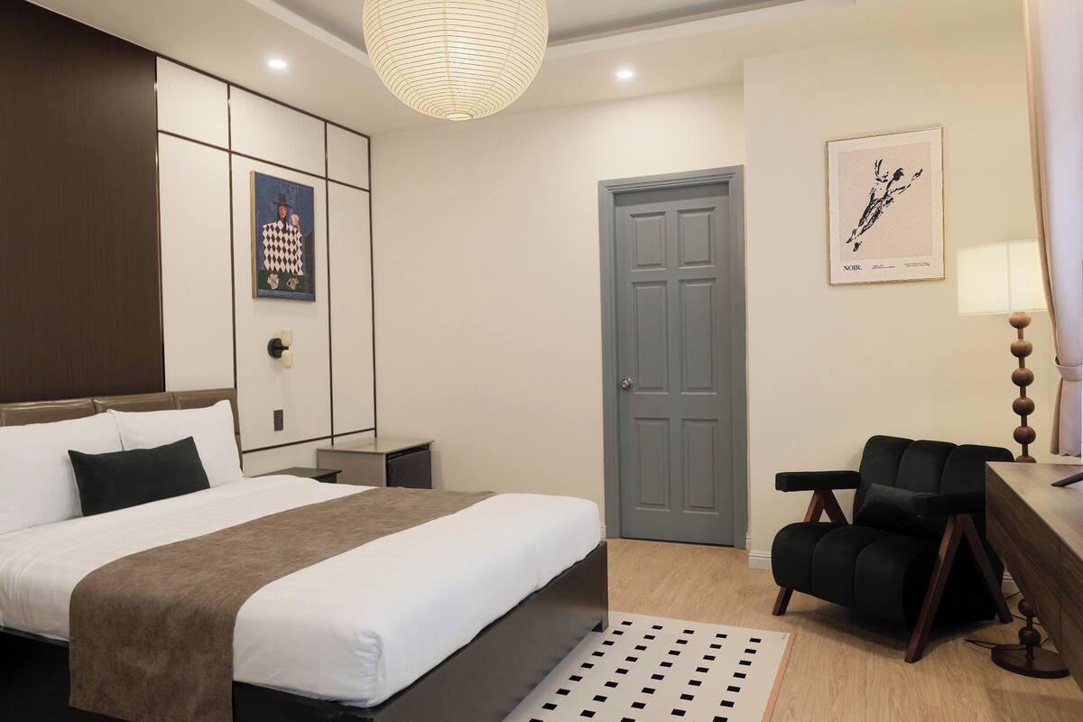 A hotel room with a bed, bedside table, desk, chair, and a door.