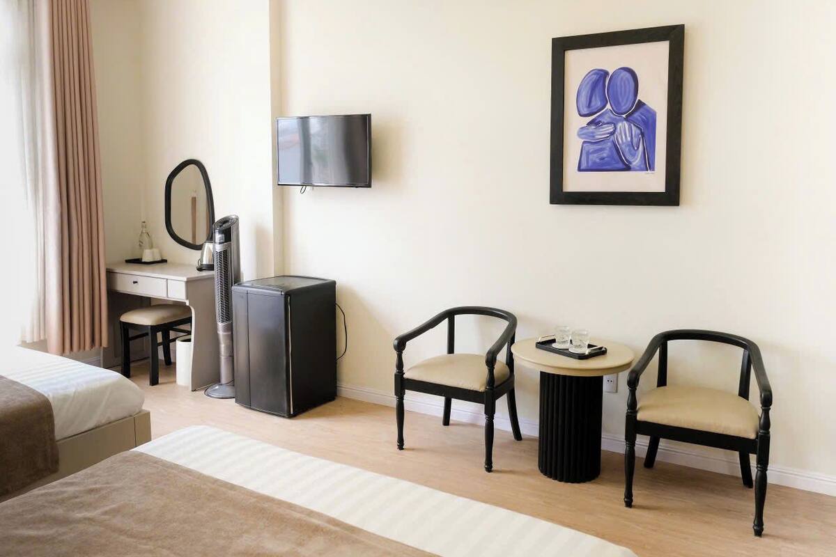 A hotel room with a bed, a desk with a chair, a TV, and a framed artwork on the wall.