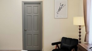 A hotel room with a bed, a black chair, a wooden dresser, a lamp, and a framed artwork on the wall. - Ngoc Trai Vang Hotel (Xuan Huong - Da Lat)