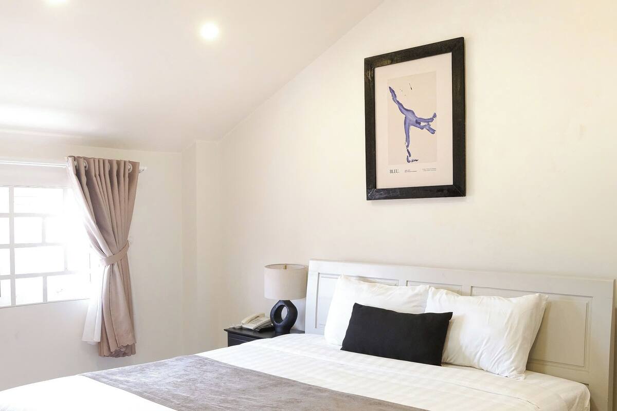 A neatly made bed with white and brown bedding, a bedside table with a lamp, and a framed picture on the wall.