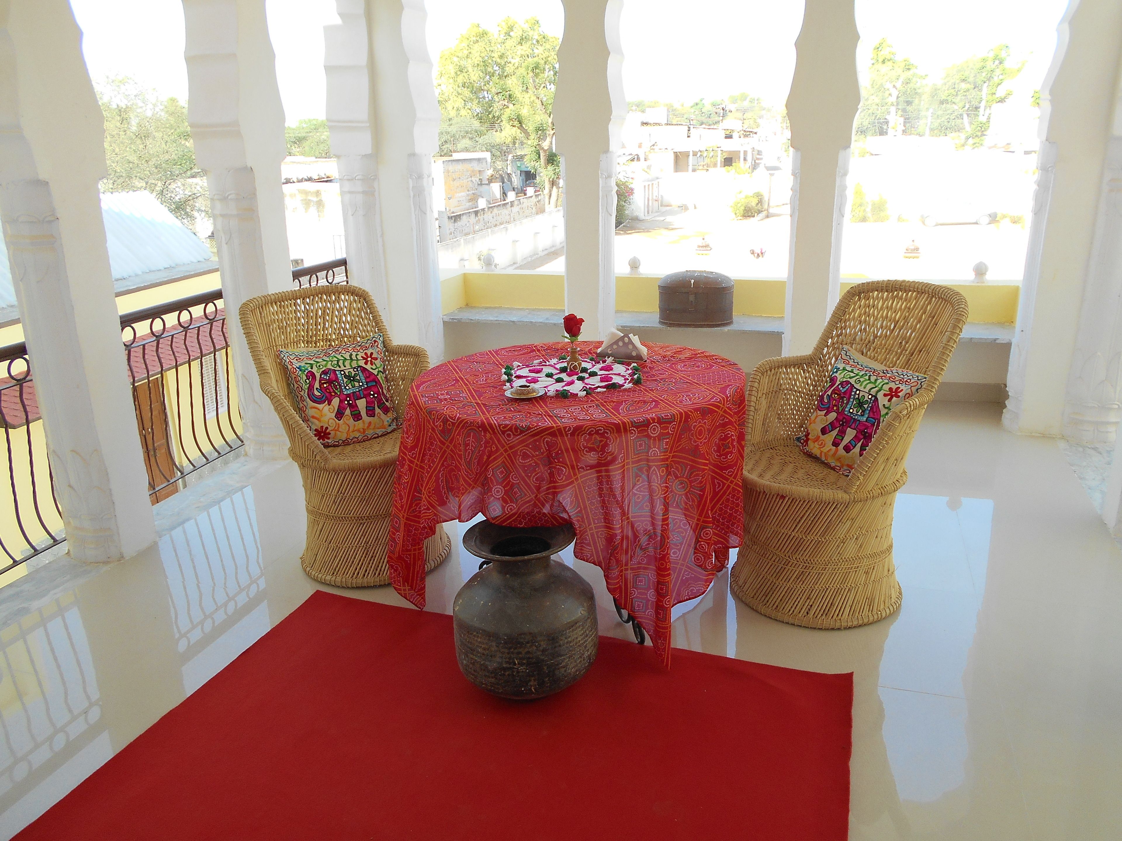 Un balcon avec une table dressée pour deux personnes, agrémentée d’une nappe rouge et d’un vase décoratif.