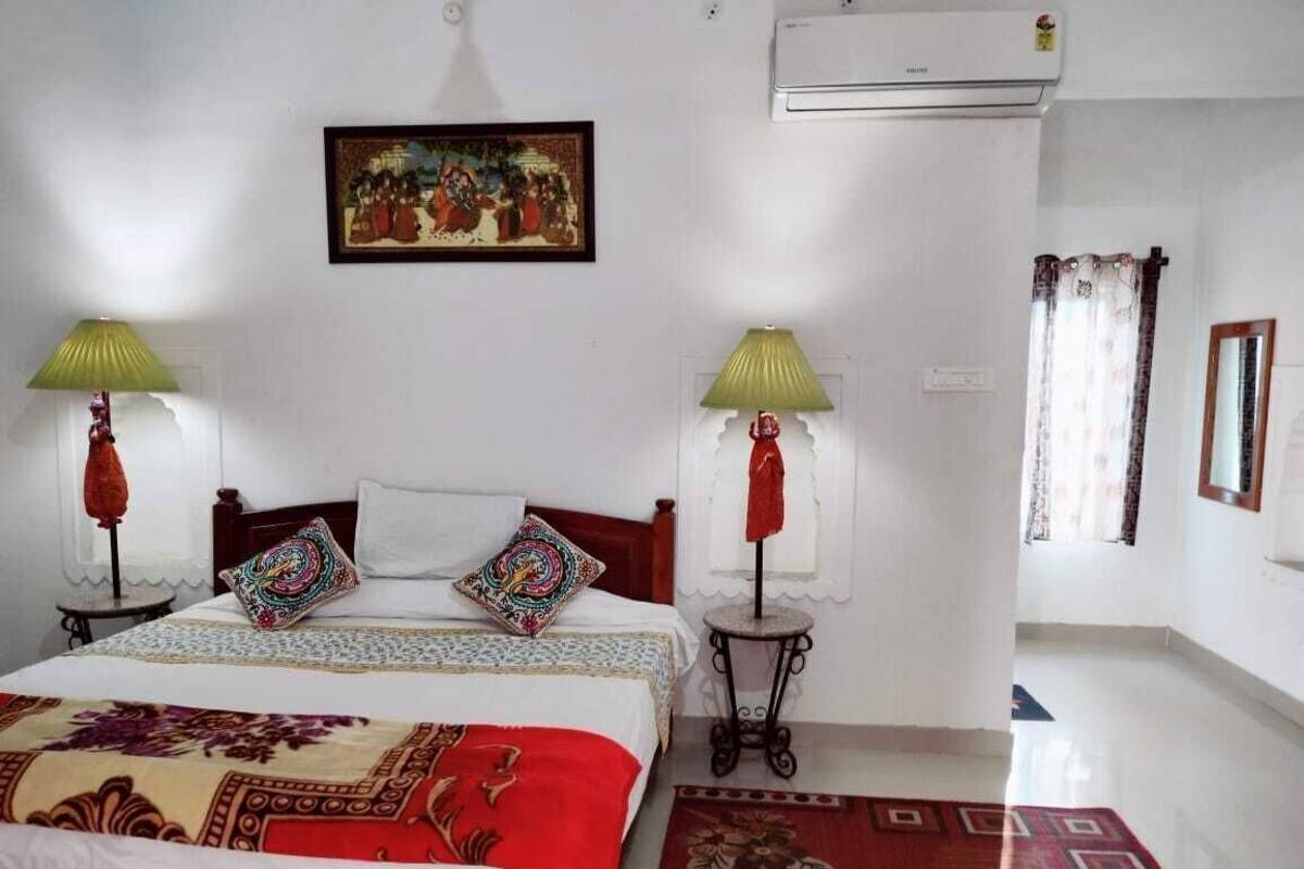 Habitación de hotel con cama, dos lámparas, un cuadro, aire acondicionado y ventana con cortinas.