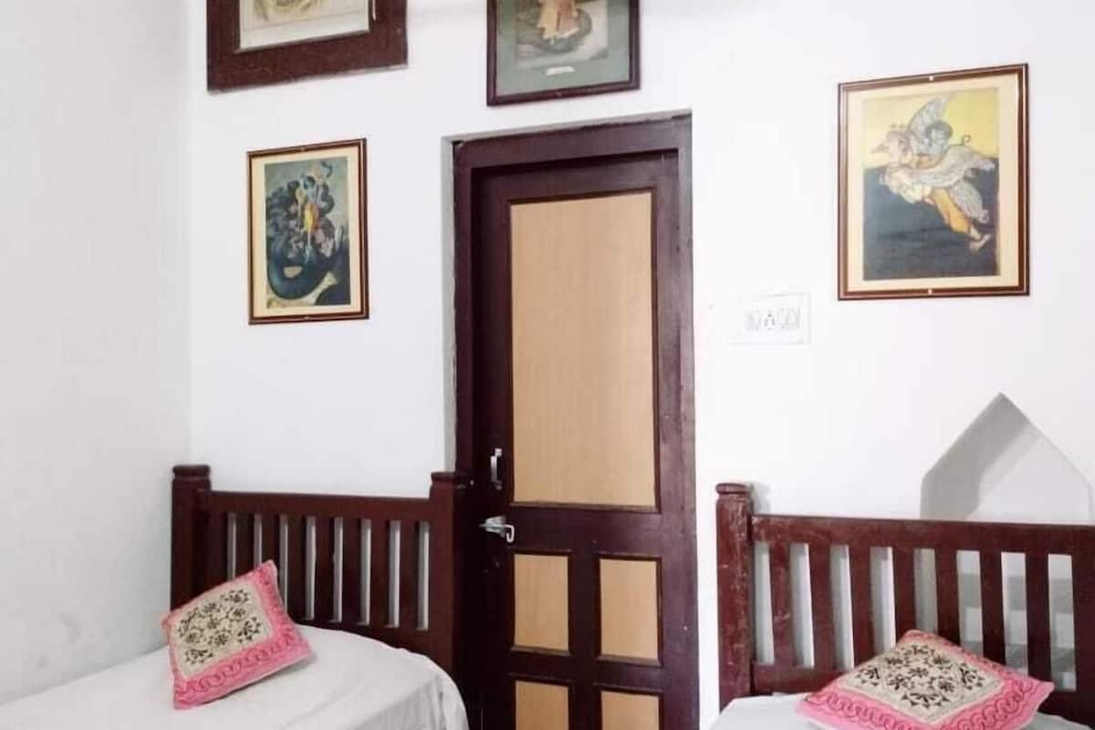 Una habitación con dos camas individuales, una puerta de madera y tres cuadros en la pared.