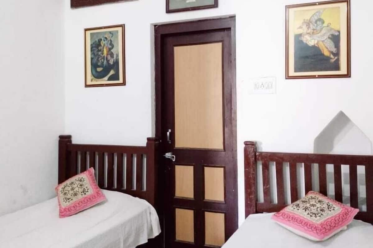 Una habitación con dos camas individuales, una puerta de madera y tres cuadros en la pared.