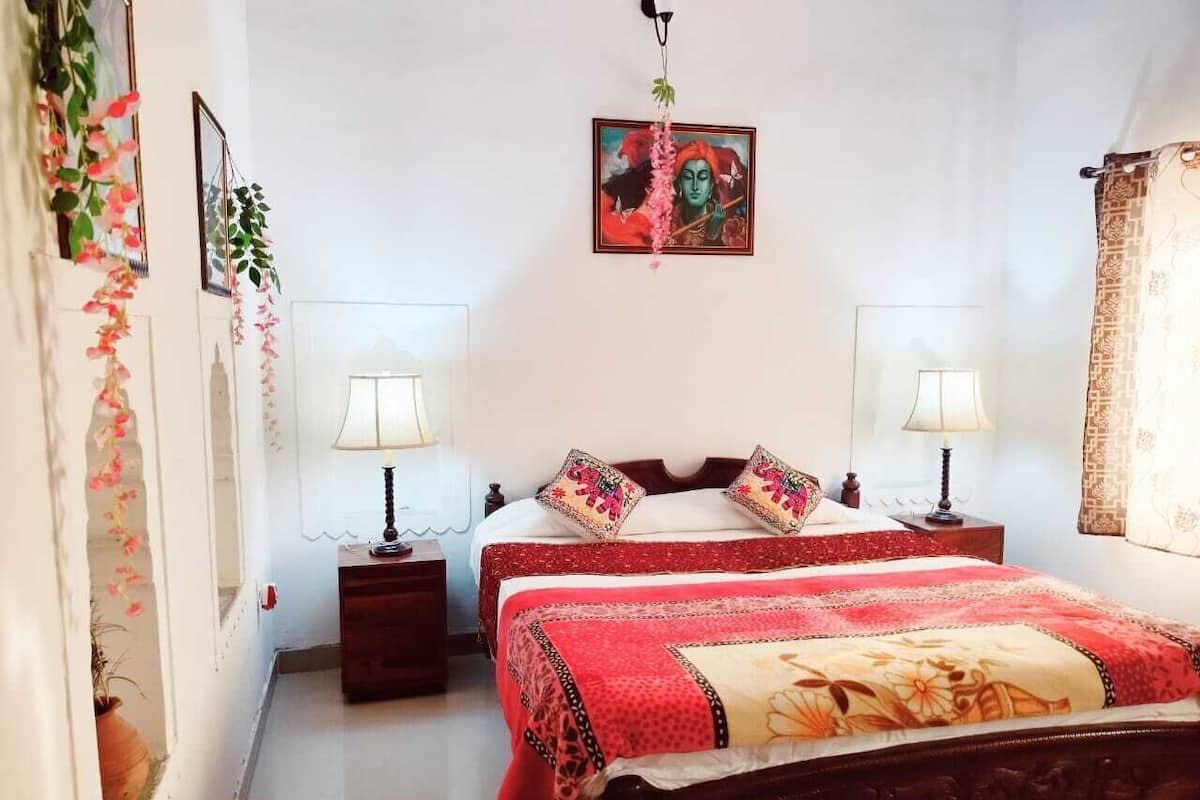 Un dormitorio con dos camas, una mesita de noche, una lámpara, un cuadro en la pared y una ventana con cortinas.