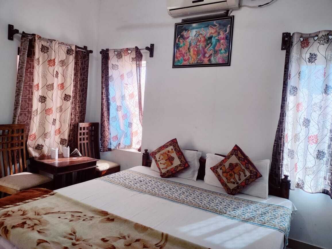 Una habitación de hotel con una cama, dos sillas, una mesita y cortinas.