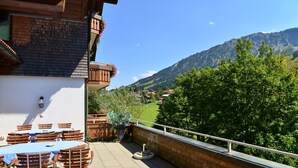 An outdoor patio with a table and chairs, a brick wall, and a view of a mountain and greenery. - Haus Jagdhof (Bad Hindelang)