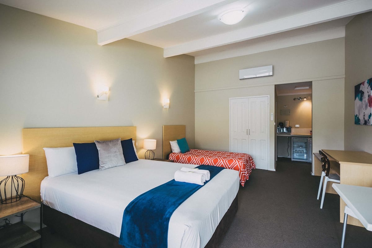 A hotel room with two beds, a desk, a chair, a kitchenette, and a bathroom.