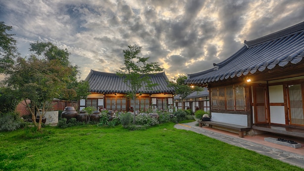 Un bâtiment de style coréen traditionnel, doté d’un jardin bien entretenu et surplombant un ciel dégagé.