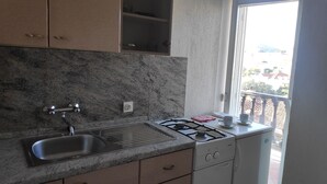 Una cocina con encimera de granito, pileta de acero inoxidable y estufa a gas. Se ve una ventana con vistas a edificios.