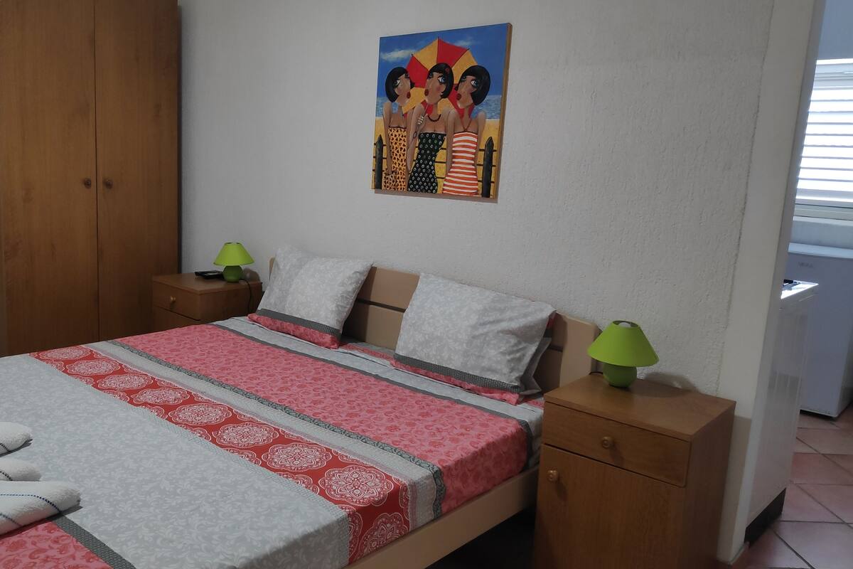 Un dormitorio con cama, almohadas, mesita de noche, lámpara, un cuadro y armario.