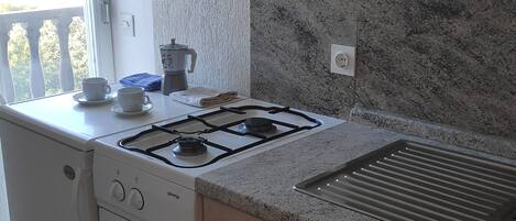 A kitchen with a gas stove, a sink, and a countertop. There are cabinets and a window with a view of the outdoors.