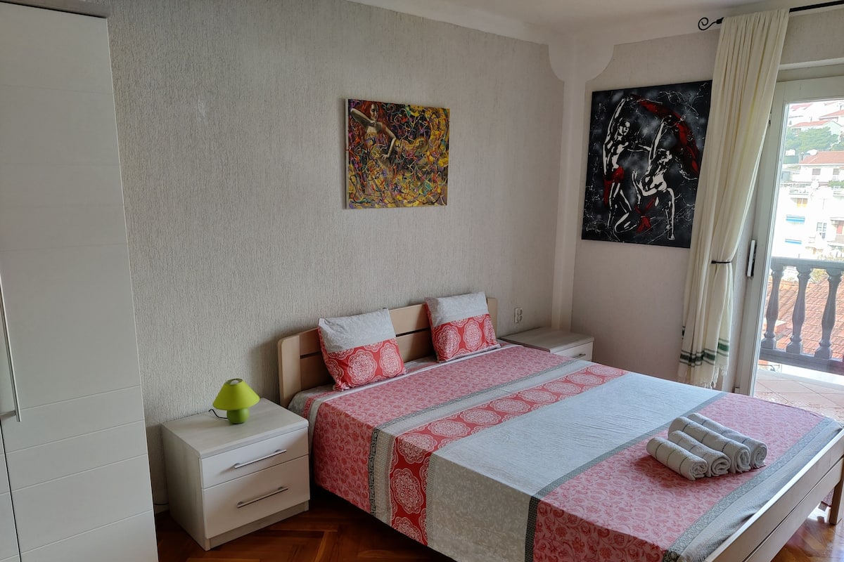 Un dormitorio con cama, mesitas de noche, lámpara y obras de arte en las paredes.