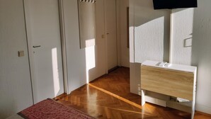 Un pasillo con suelo de madera, paredes blancas y un televisor montado.