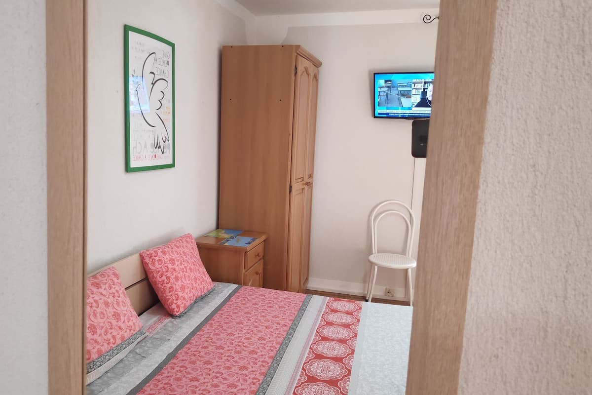 Un dormitorio con cama, armario de madera, escritorio pequeño, silla, televisor en la pared y una obra de arte enmarco.