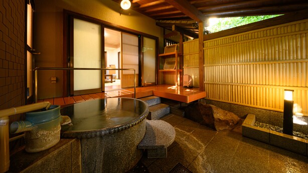 Uma onsen japonesa tradicional com banheiras de pedra, bancos de madeira e piso de tatame.