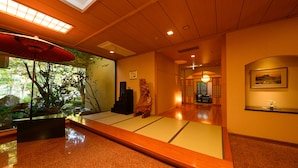 Interior japonês tradicional com tatames, teto de madeira e vista para o verde lá fora.