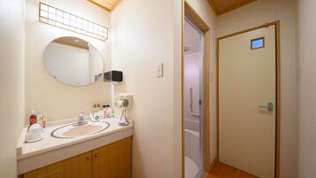 A bathroom with a sink, mirror, and a door leading to a shower.