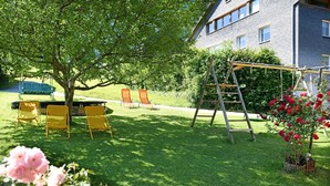A grassy yard with a swing set, yellow chairs, and a ladder.