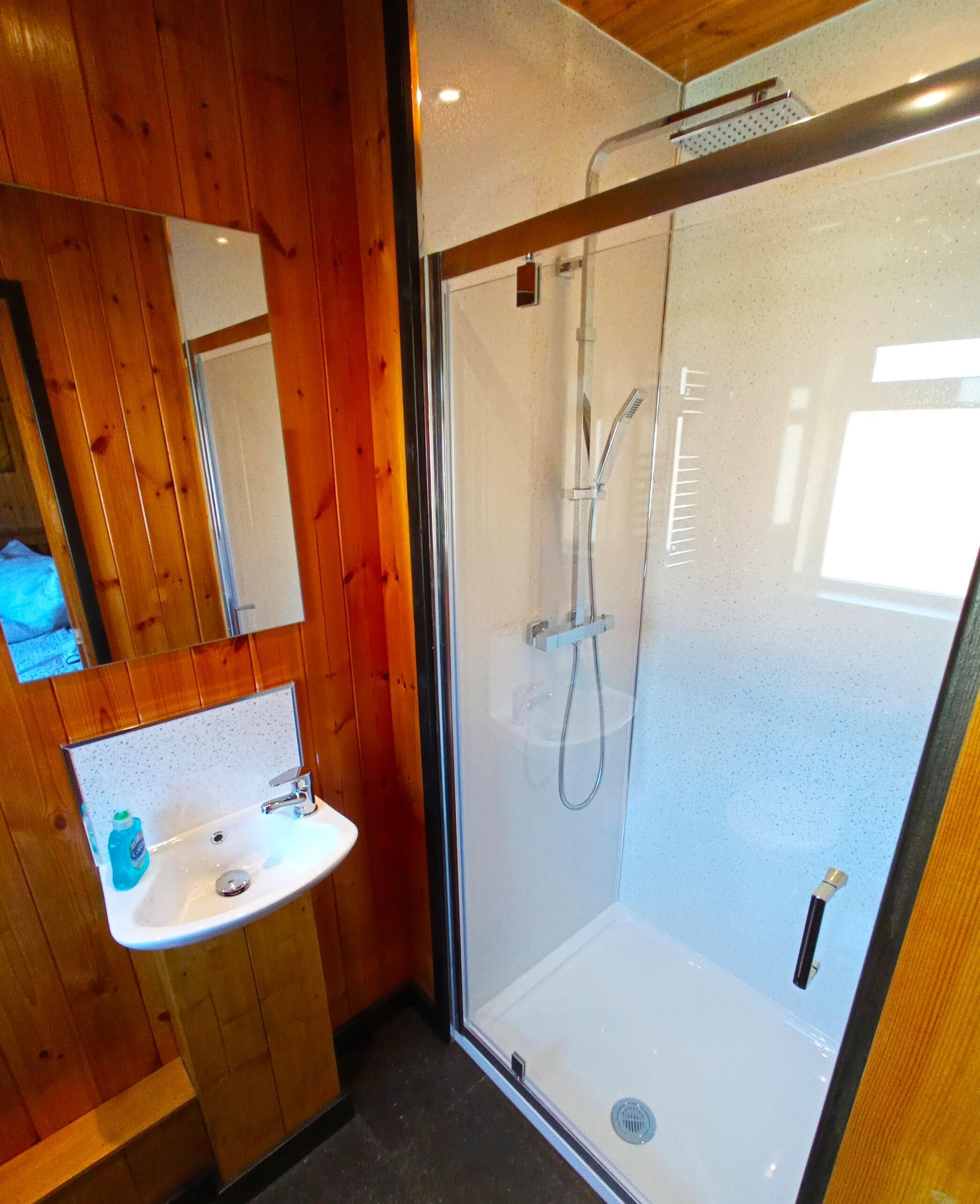 A bathroom with a wooden interior, a glass-enclosed shower, and a white sink with a mirror above it.