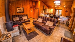 A cozy cabin interior with a fireplace, leather sofas, a dining table, and a kitchen area. - New Forest Lodges (Wimborne)