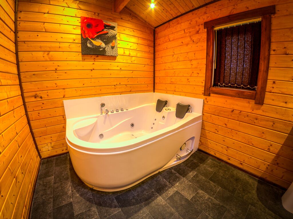 A wooden cabin bathroom with a white bathtub, a pop art painting on the wall, and a window with curtains.