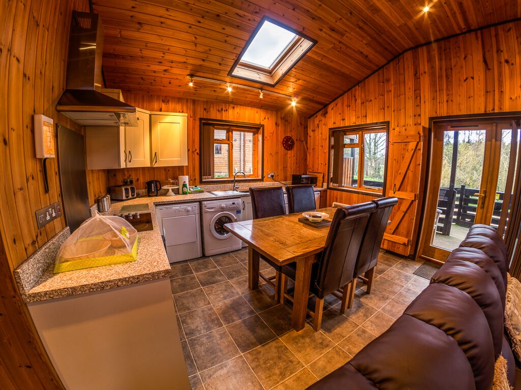A cozy cabin interior with a wooden interior, a dining area with a table and chairs, a kitchen with appliances, and a large window.