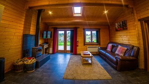 A cozy log cabin interior with a fireplace, leather sofa, and a television. - New Forest Lodges (Wimborne)