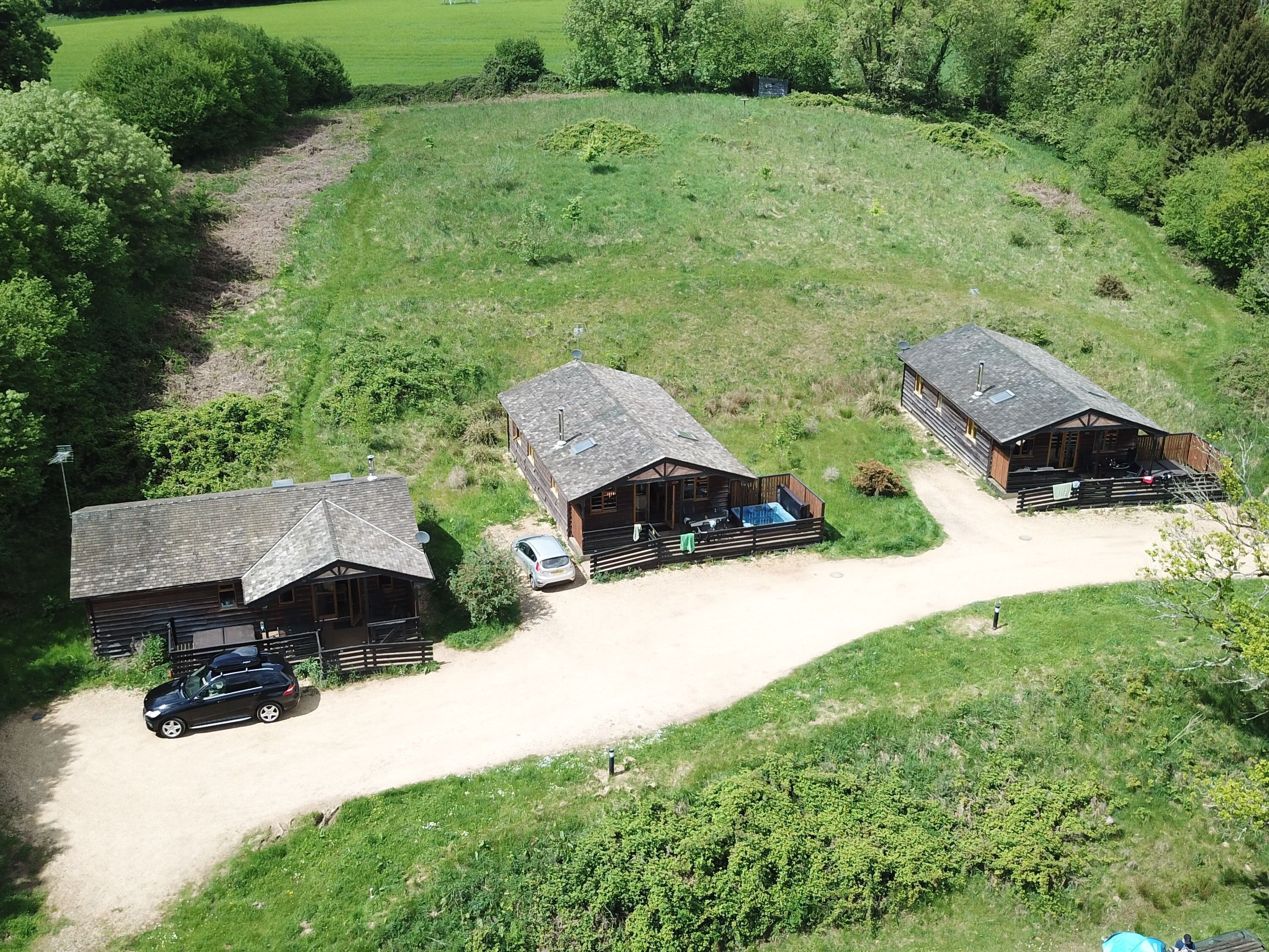 A rustic lodge with three cabins, each featuring a sloped roof and wooden exterior. A dirt path connects the cabins, and a car is parked near the middle cabin.