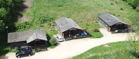 A rustic lodge with three cabins, each featuring a sloped roof and wooden exterior. A dirt path connects the cabins, and a car is parked near the middle cabin.