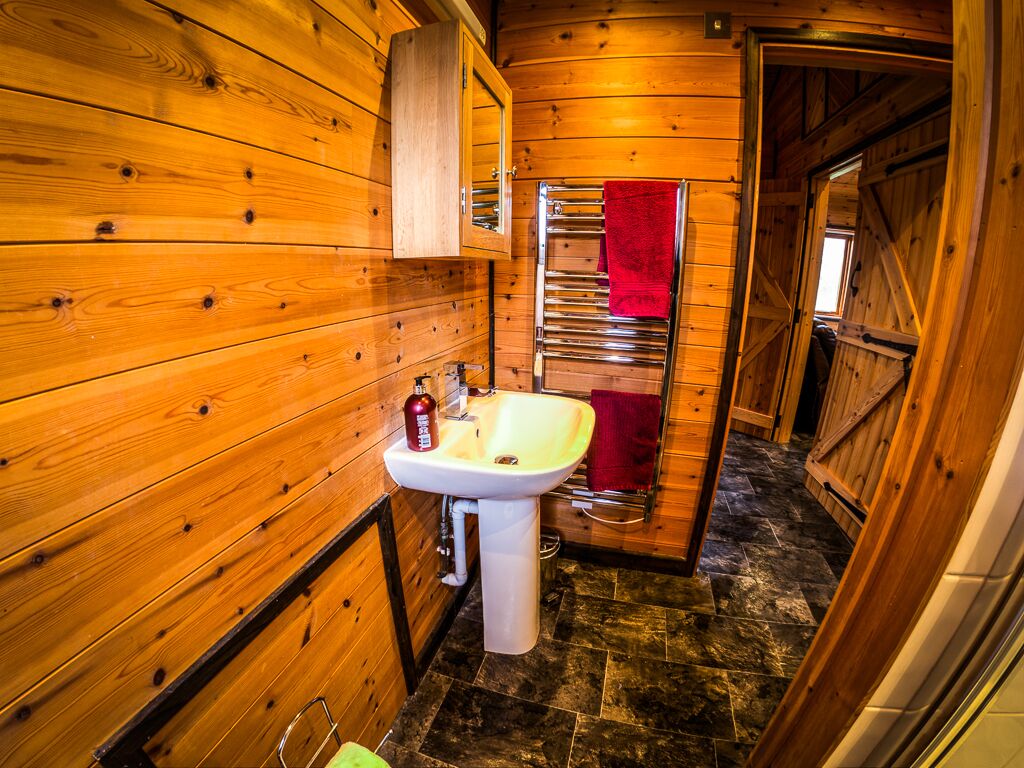 A wooden cabin bathroom with a sink, mirror, and towel rack.