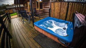 A wooden cabin with a hot tub on a wooden deck. - New Forest Lodges (Wimborne)