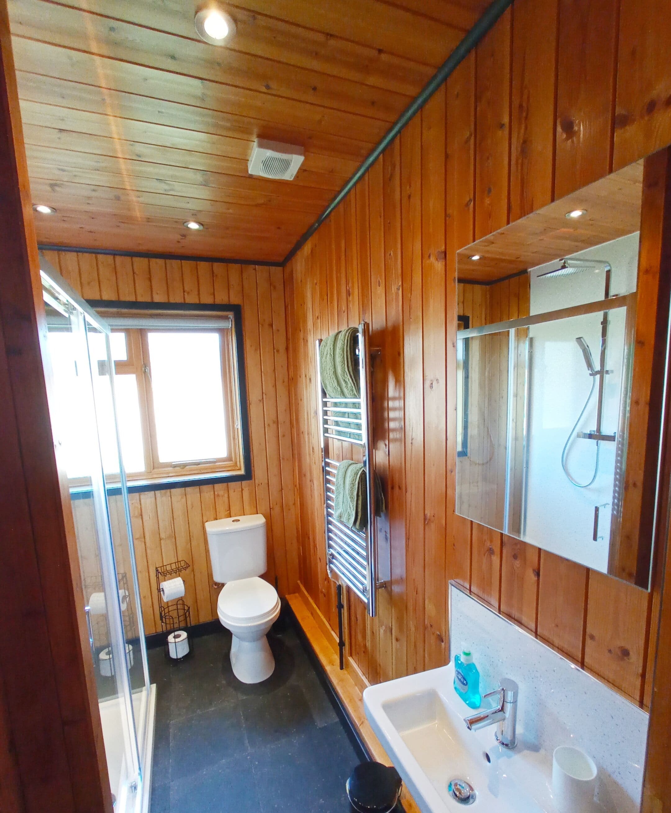 A wooden-paneled bathroom with a toilet, sink, and shower.