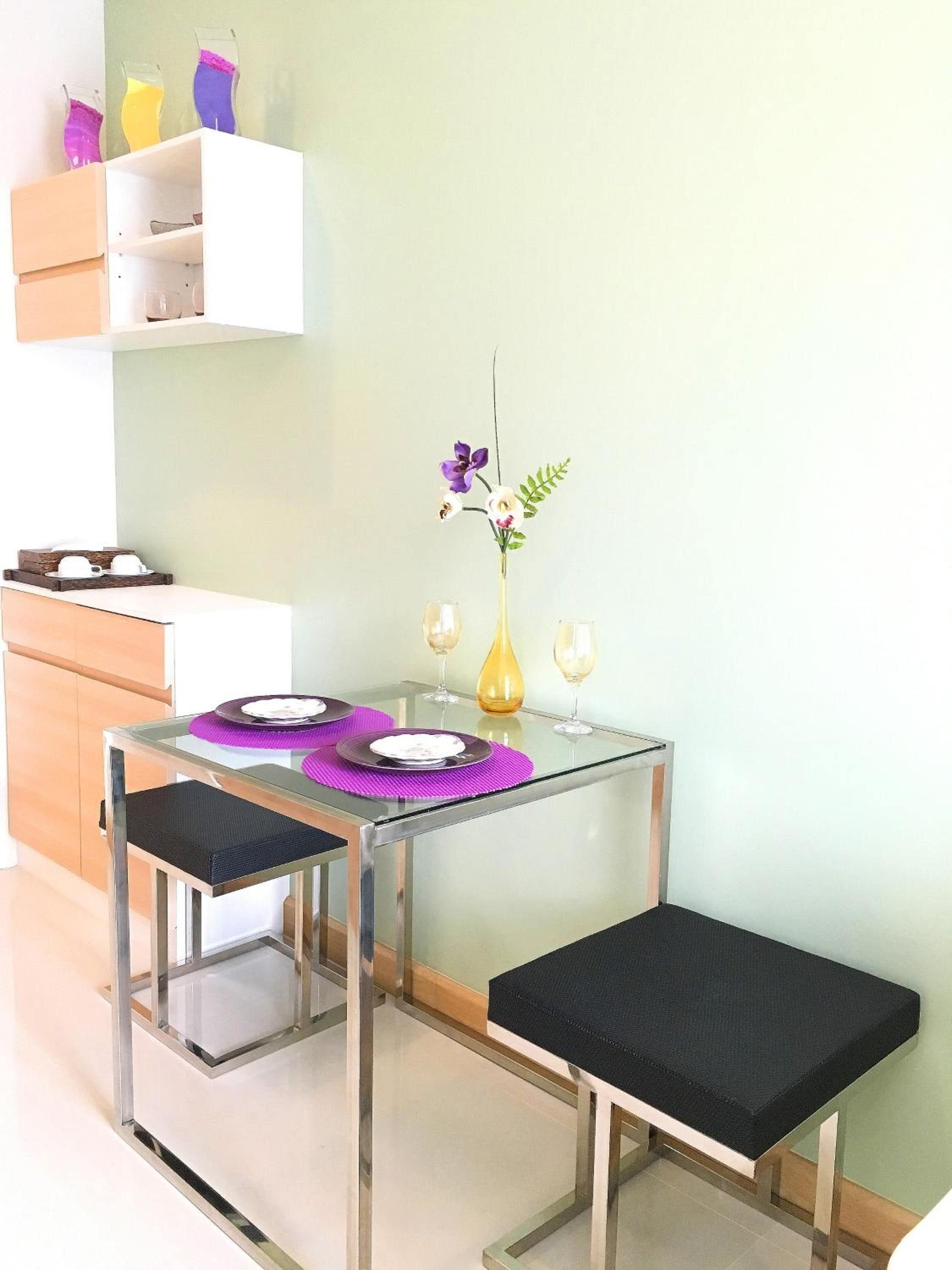 A modern kitchen with a glass table set for two, a vase with flowers, and a shelf with colorful containers.