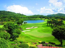 Un campo de golf con un lago, rodeado de exuberante vegetación y colinas.
