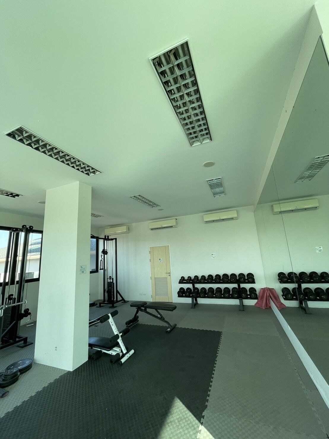 A gym with exercise equipment, a mirrored wall, and a rack of dumbbells.