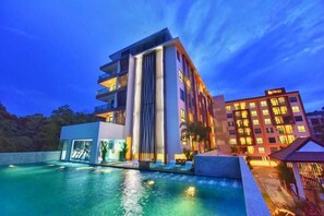 Un hotel moderno con piscina, varios balcones y una fachada bien iluminada.