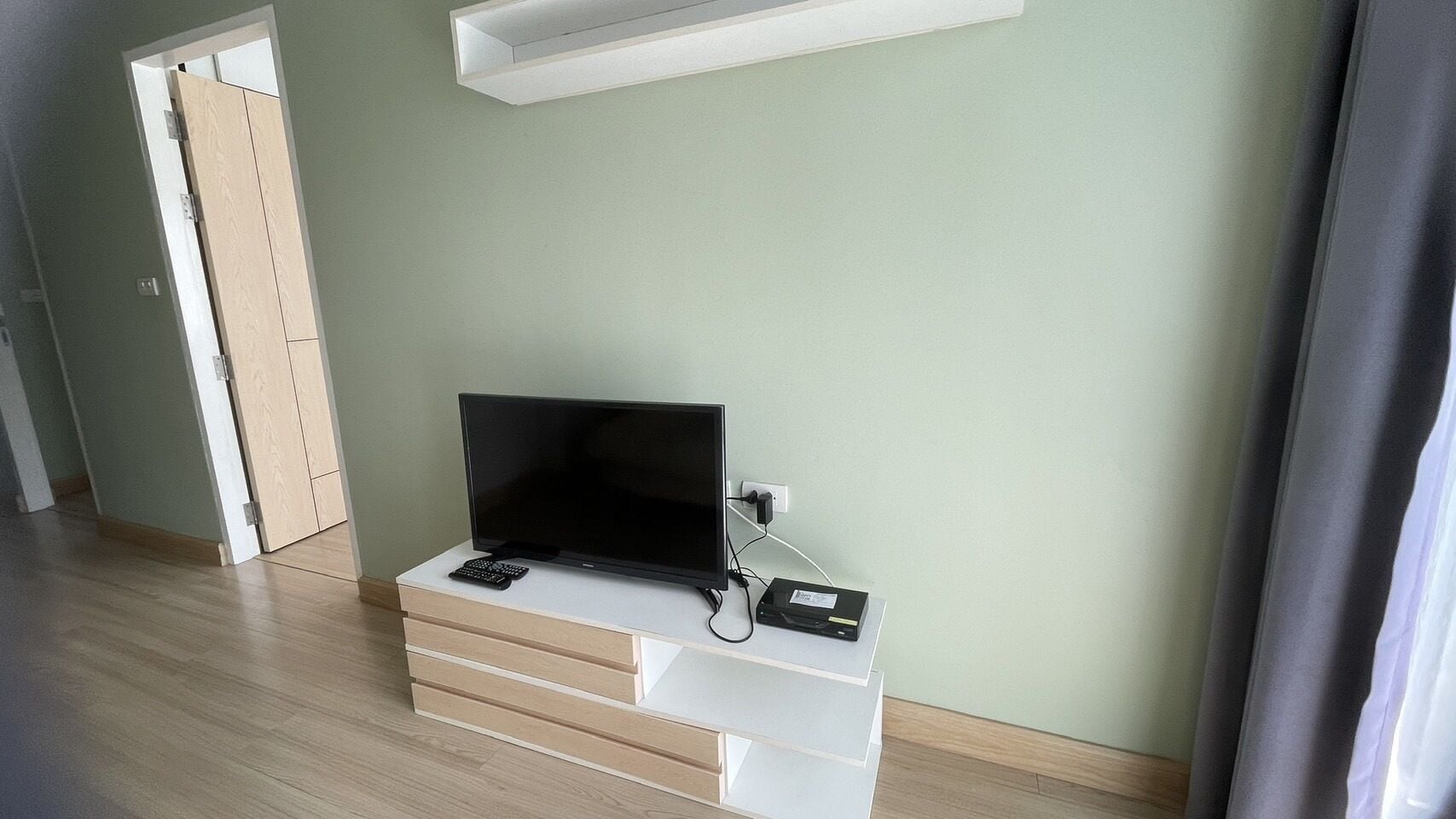 Una habitación con una televisión de pantalla plana sobre un mueble blanco, un control remoto y una regleta de enchufes.