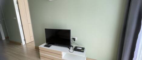 Una habitación con una televisión de pantalla plana sobre un mueble blanco, un control remoto y una regleta de enchufes.