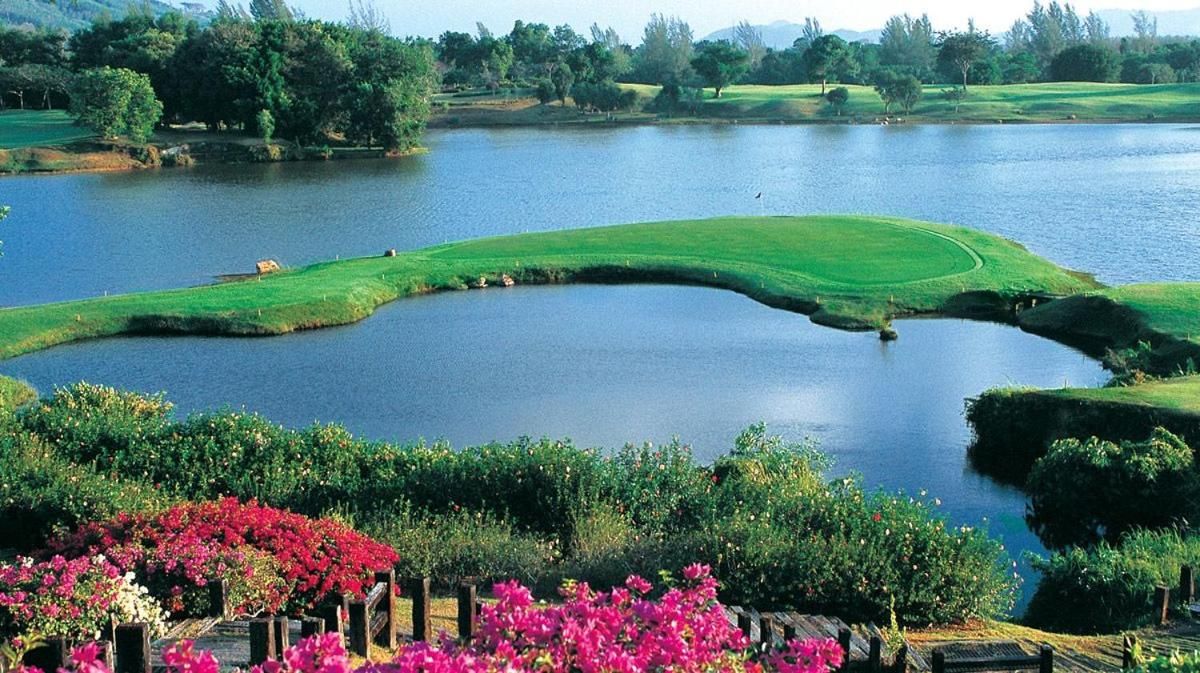 Golfkenttä, jonka yhteydessä on vesialue, ja jota ympäröi vehreä kasvillisuus ja kukkivat kasvit.