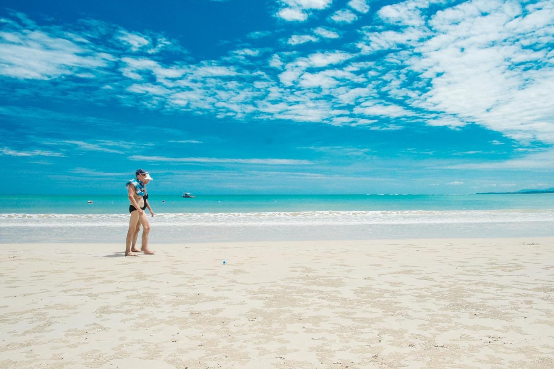 Escena de playa con una persona de pie sobre la arena, cielo despejado y el océano al fondo.